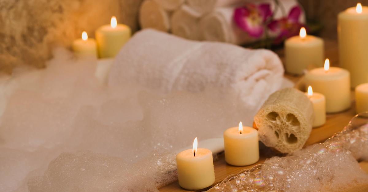 Candles and natural loofa at the edge of a bubble bath with a towel for pillow