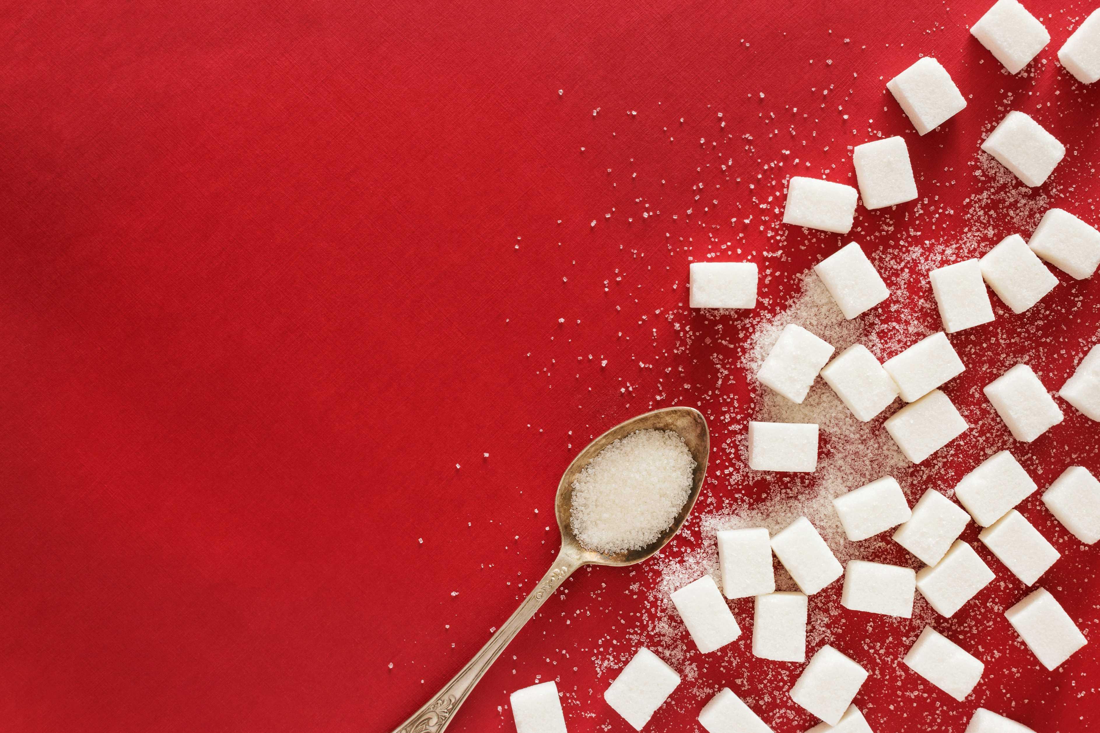 A spoon full of sugar lays on a red placemat beside white sugar cubes.