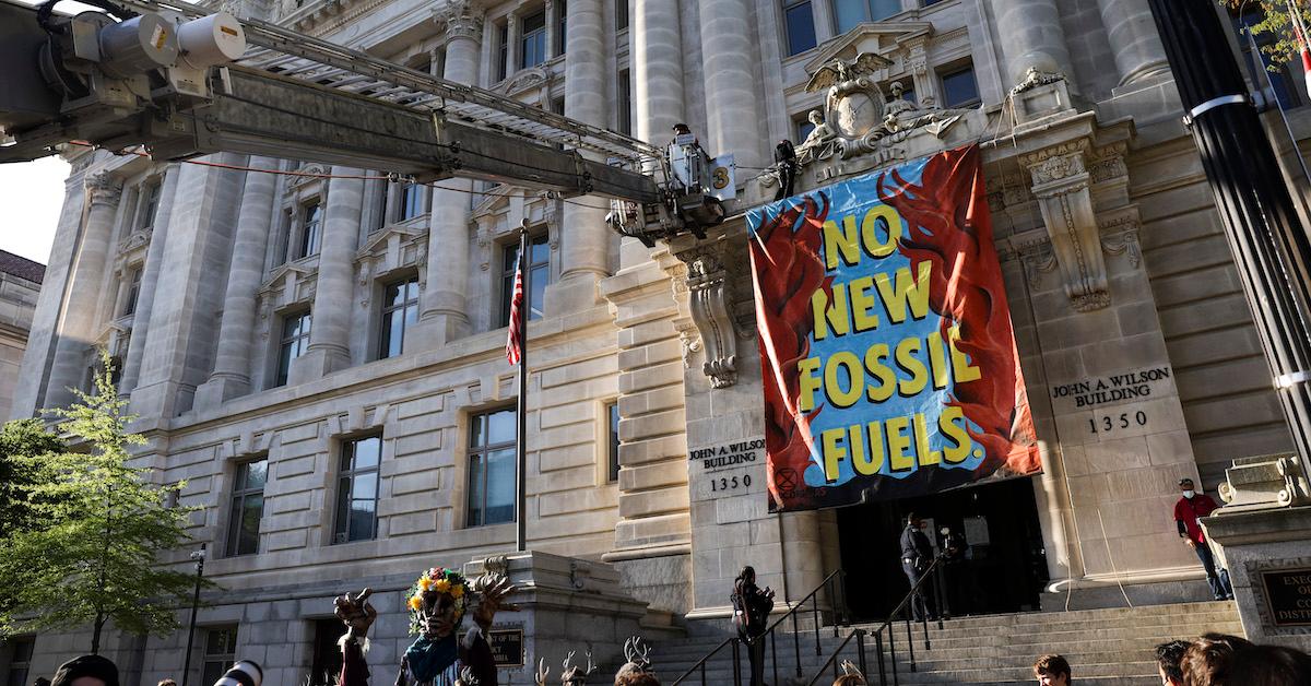 A crane attempts to remove an activist from the Wilson Building in Washington, D.C., where a large banner reading “NO NEW FOSSIL FUELS” hangs.