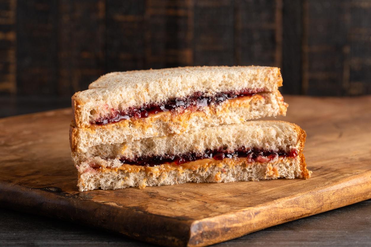 A peanut butter and jelly sandwich is pictured atop a wooden cutting board.