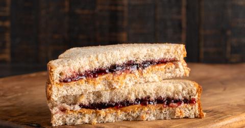 A peanut butter and jelly sandwich is pictured atop a wooden cutting board.