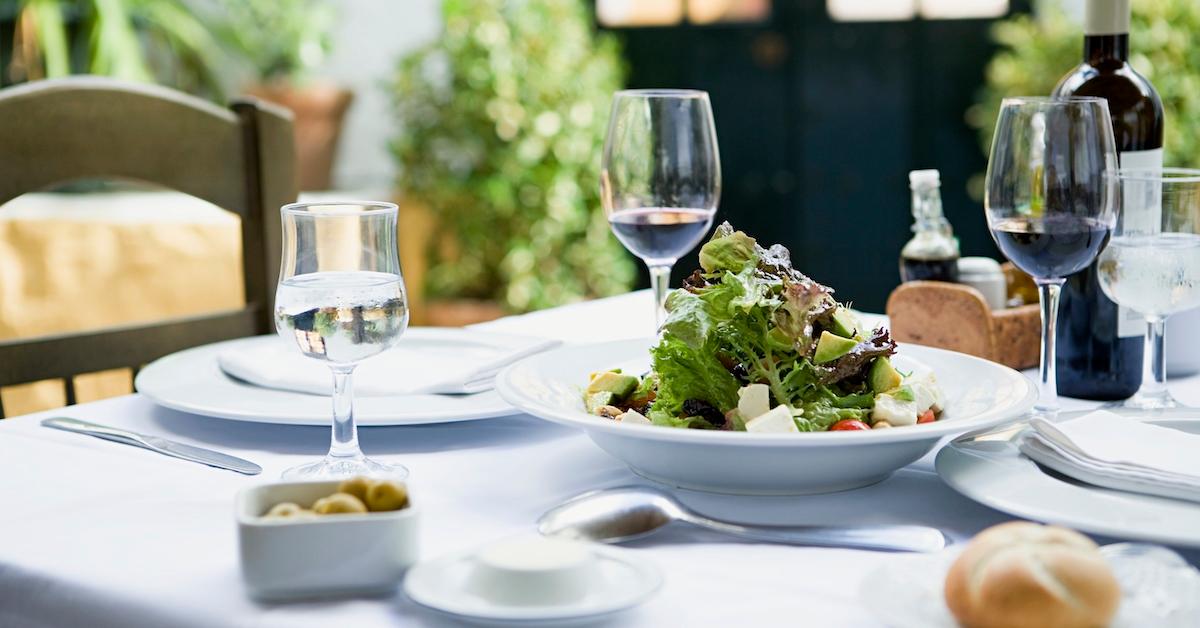 A table featuring a white tablecloth, wine glasses, and a salad