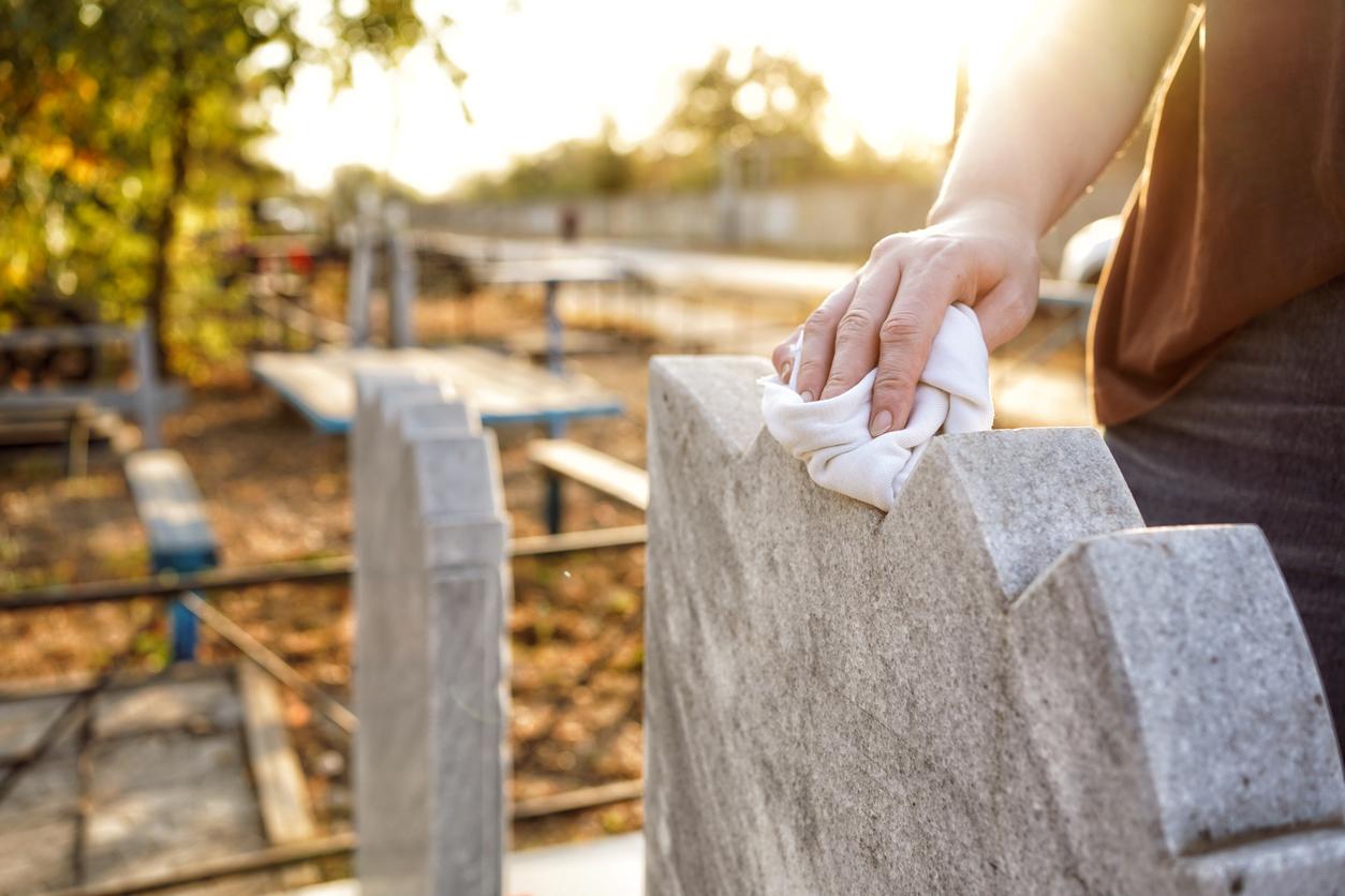 A person wipes the top of a granite headstone with a white cloth.