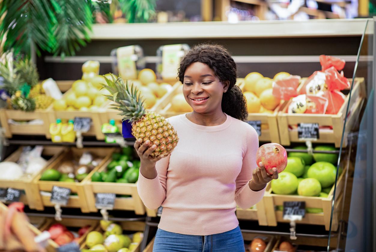 A smiling woman compares a pineapple in one hand with a pomegranate in another hand.