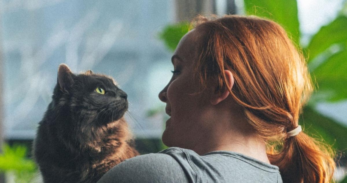 A red-haired woman holding a gray cat.