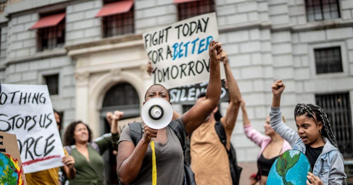 Climate protesters hold up signs and yell through a megaphone on a city street. 