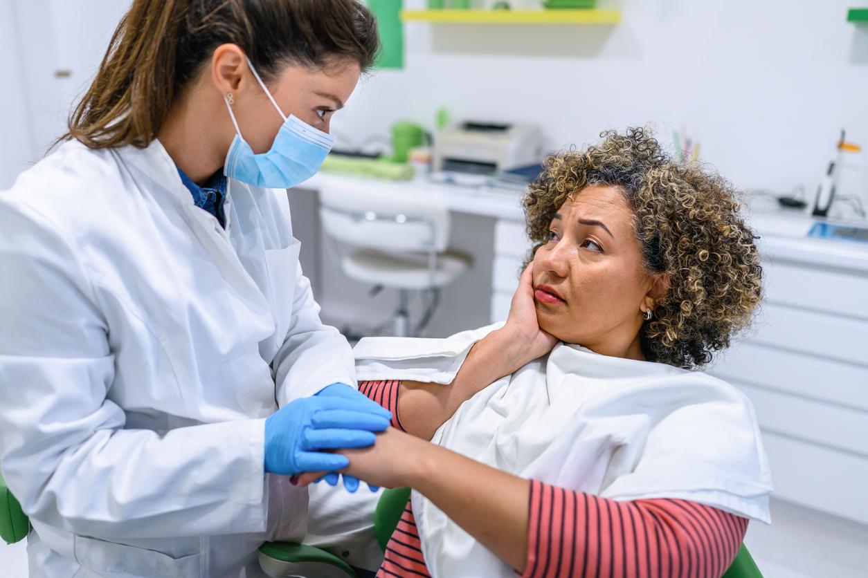 A woman indicates pain on the side of her mouth to her female dentist.