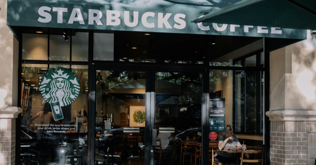 A woman sits in front of a Starbucks storefront enjoying a coffee