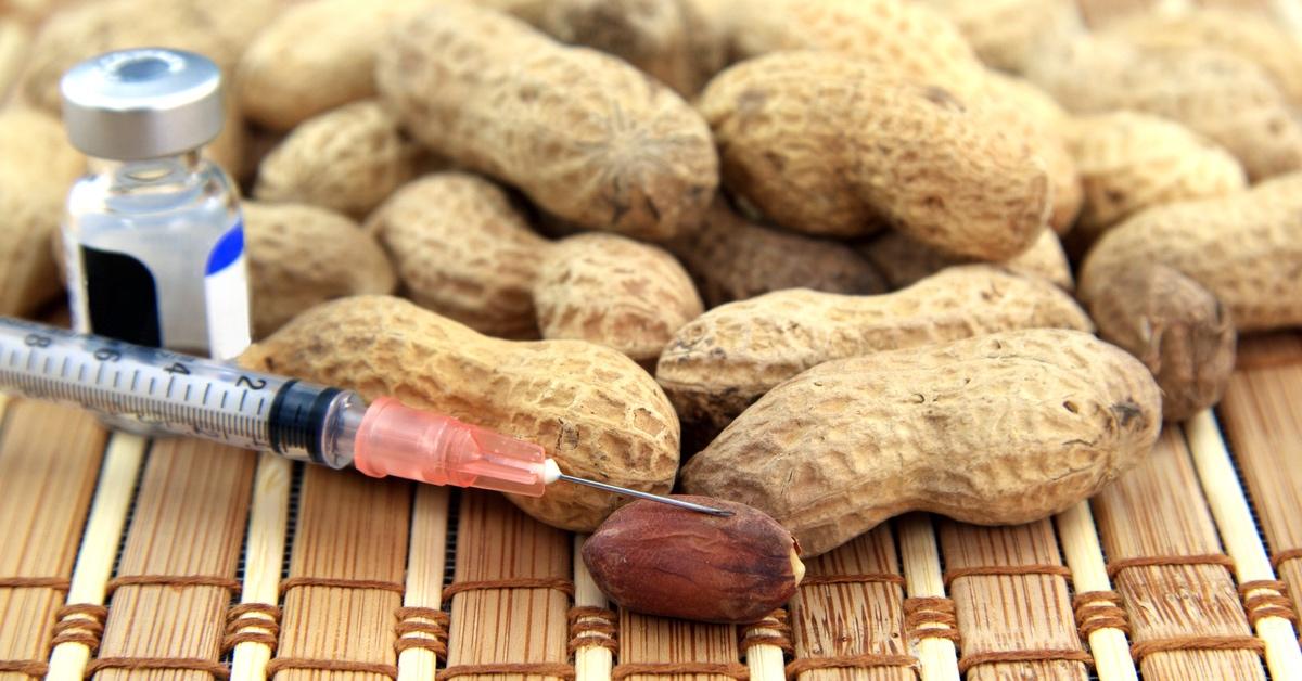 Cluster of peanuts on a wooden mat with allergy medication injection in a needle.