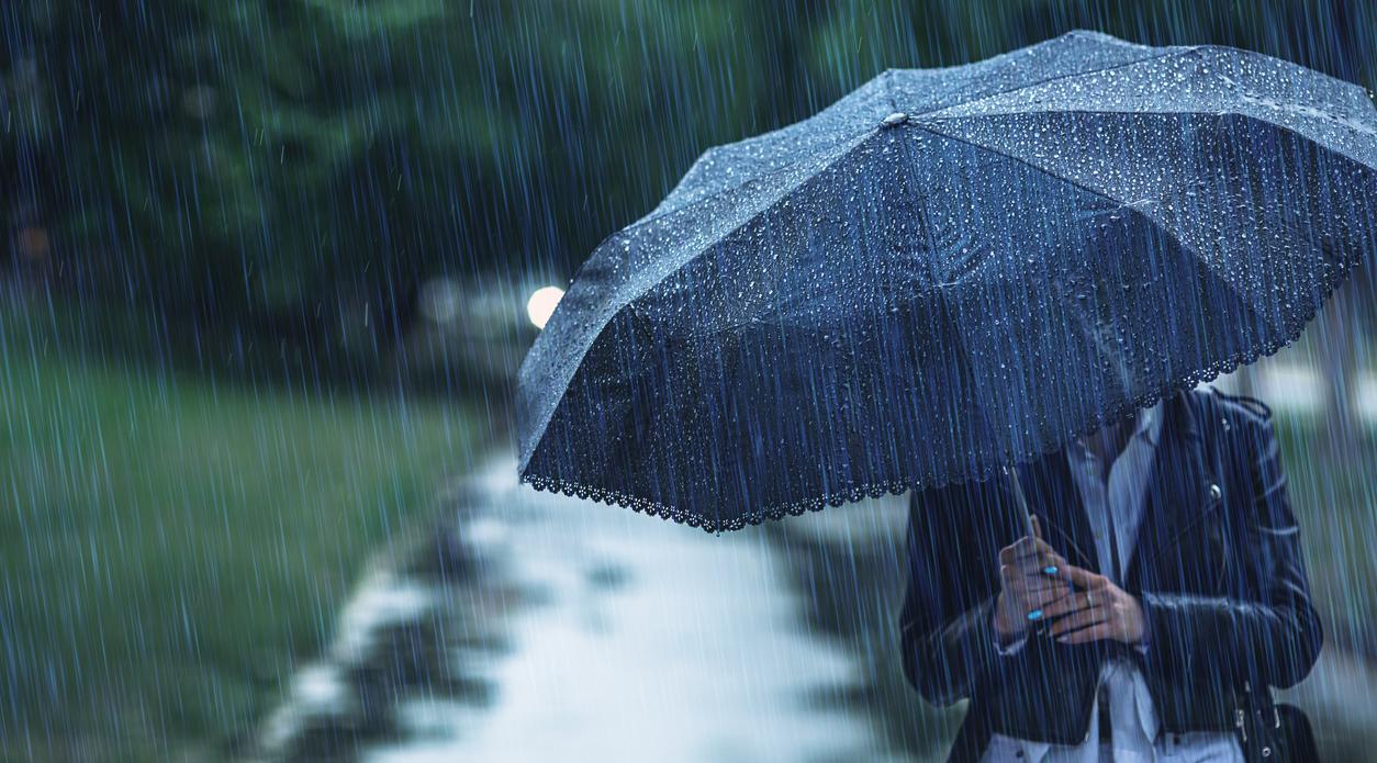 A dark umbrella shielding someone from heavy rainfall. 