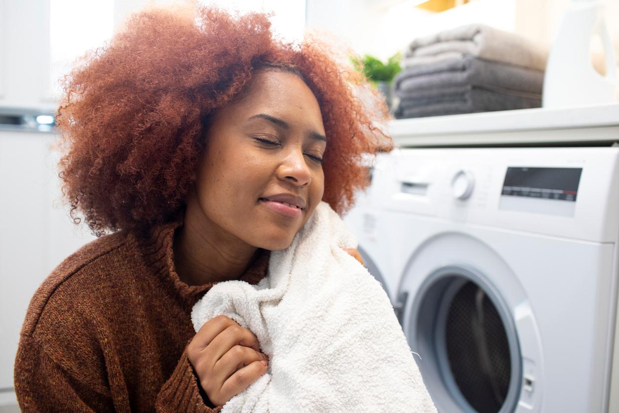 A smiling woman in a brownish and reddish sweater holds a white blanket next to an open dryer.