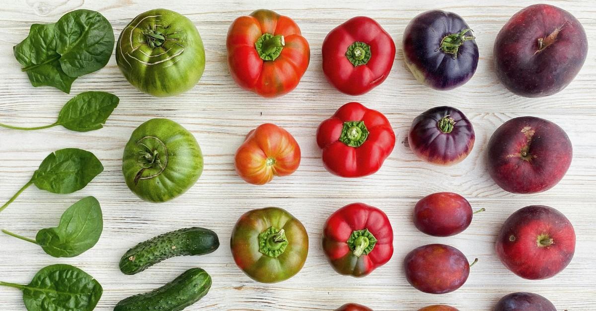 Basil, cucumbers, tomatoes, and plums are lined up on gray and white wood planks