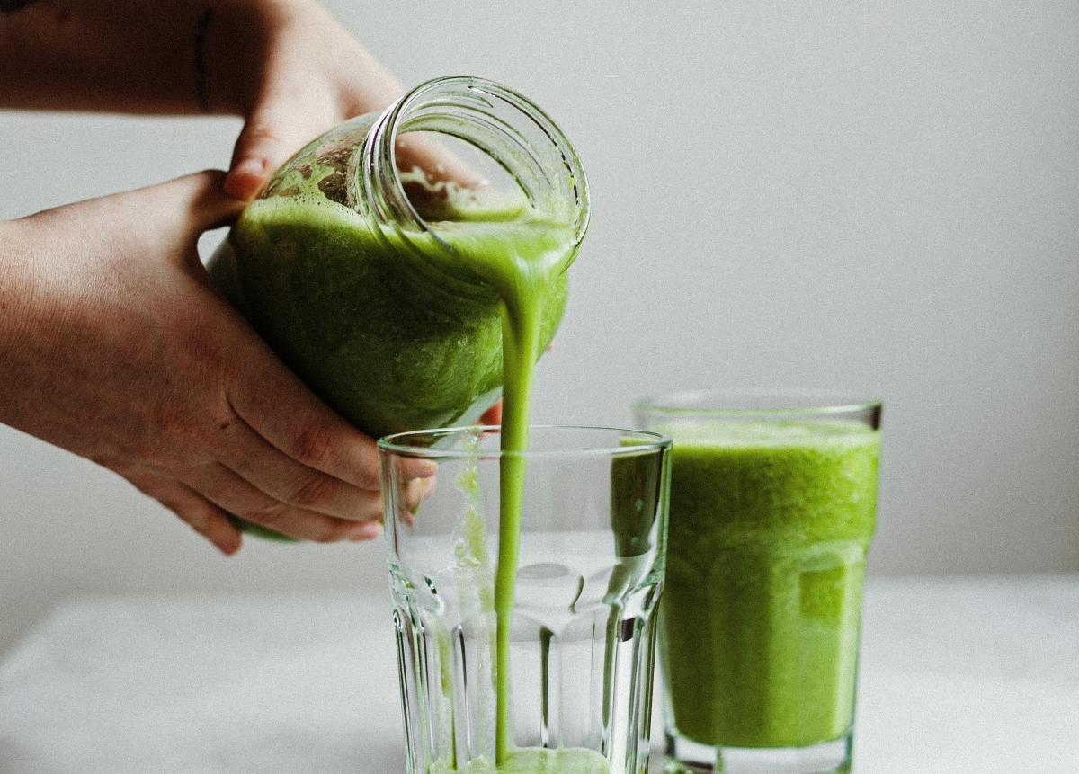 person pouring green smoothies into glasses