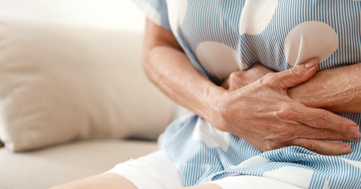 Older person wearing a blue and white shirt holding their stomach. 