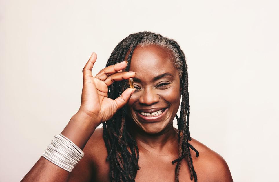 Woman holding an omega-3 fatty acid capsule to her eye. 