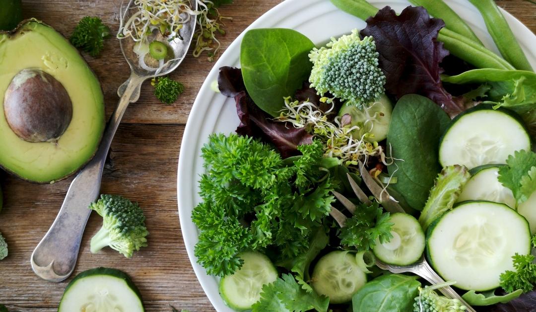 A plate of green vegetables, including cucumbers, spinach leaves, broccoli and avocado