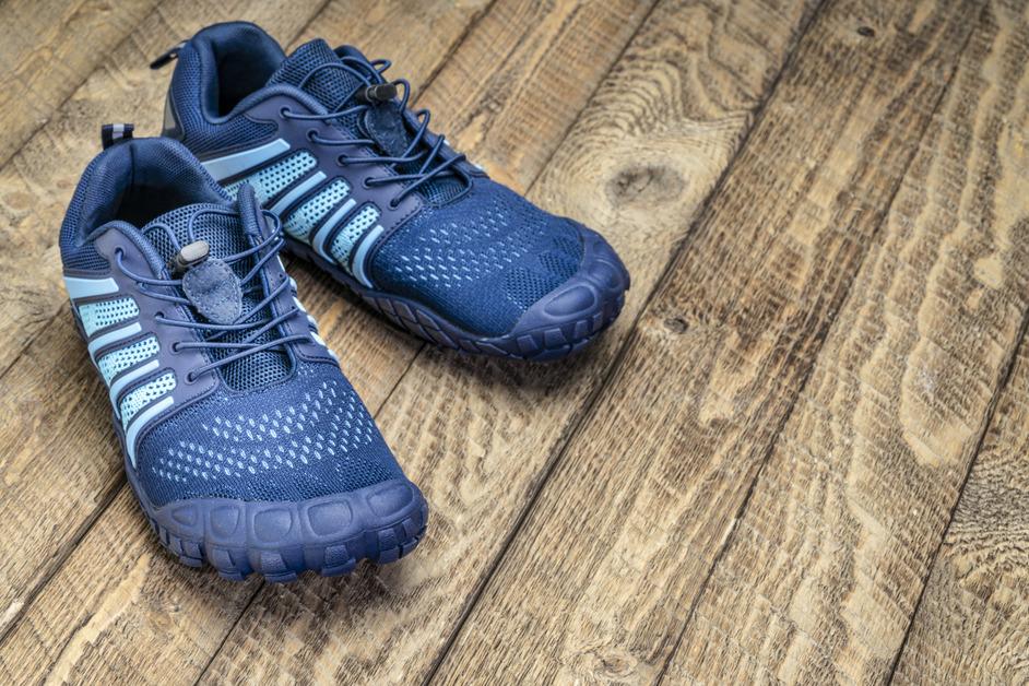 A pair of blue crossfit barefoot shoes sit on a wooden surface. 