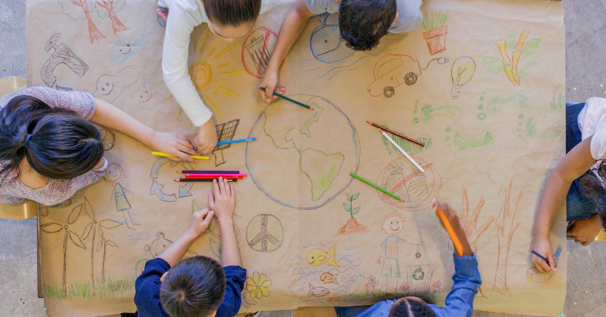 An aerial view of a group of children drawing on a piece of butcher paper