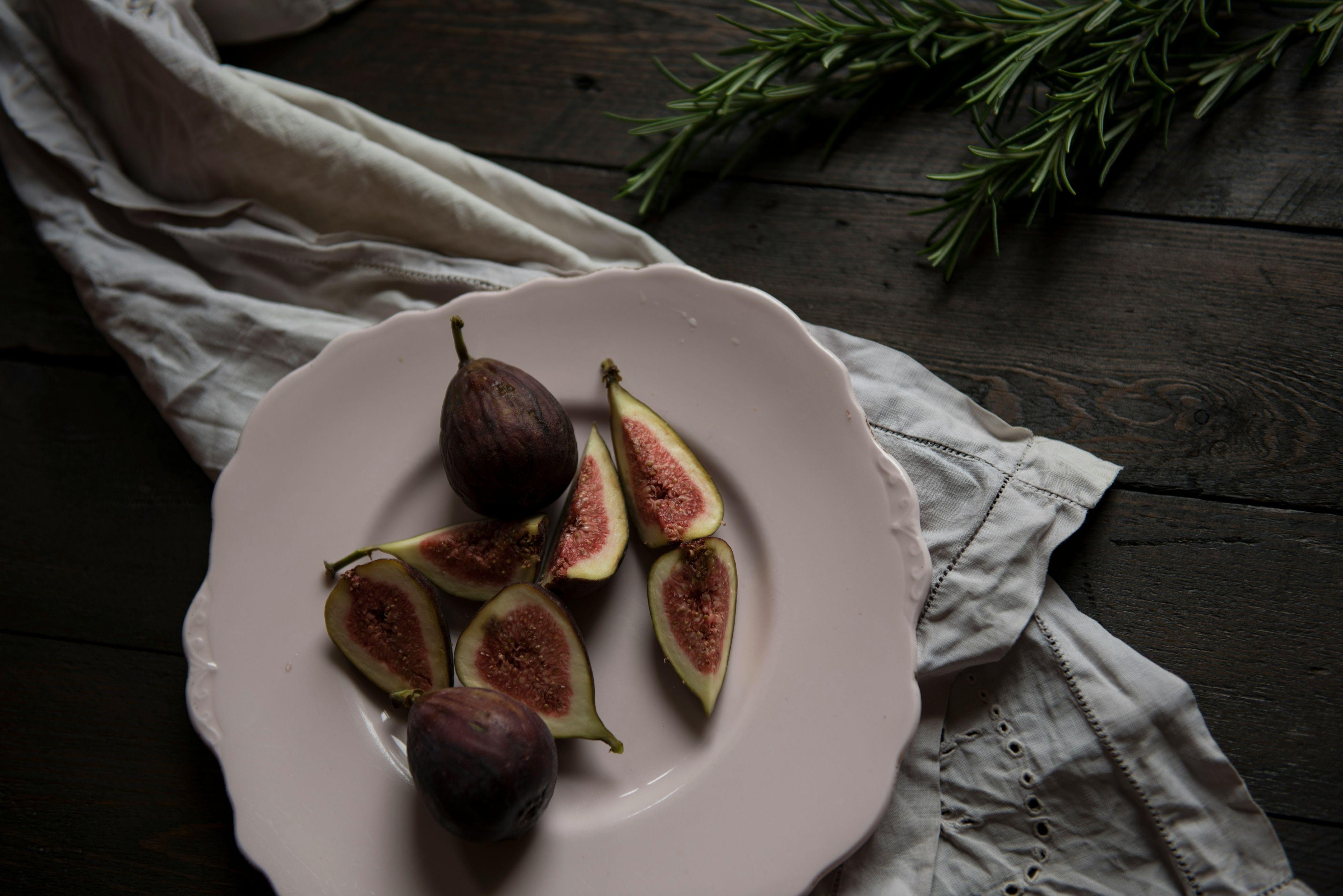 Sliced figs and whole figs are placed on a plate atop a white napkin above a dark wooden table.