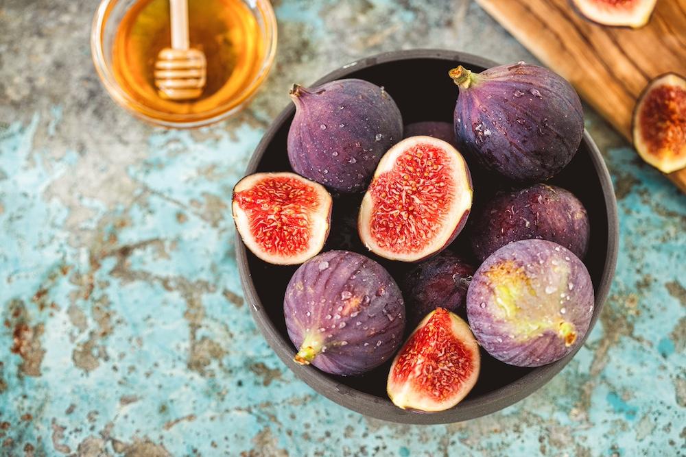 A bowl of cut figs next to honey.