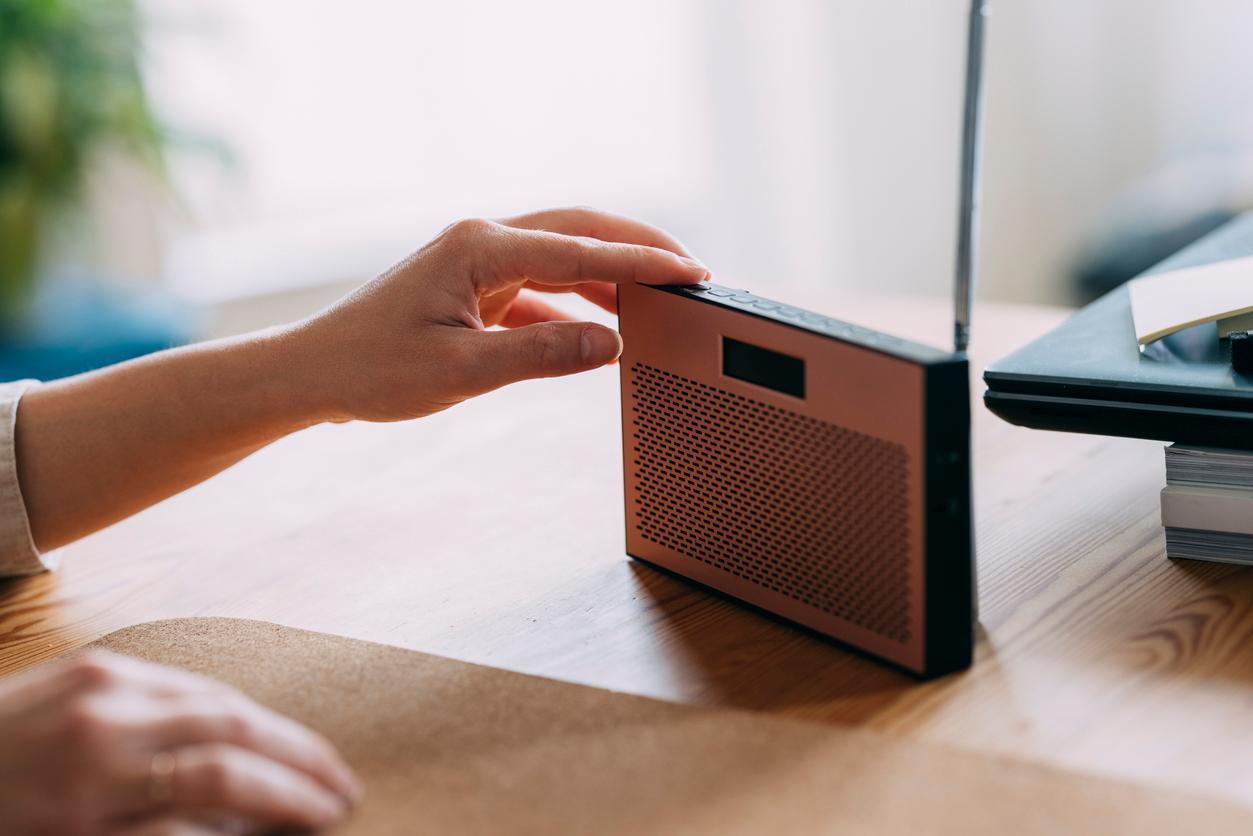 A person adjusts the buttons on a compact radio atop a wooden table.