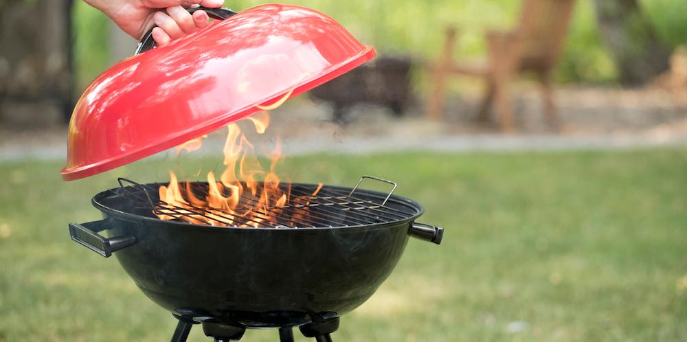 A person lifting the lid of a flaming grill outside. 