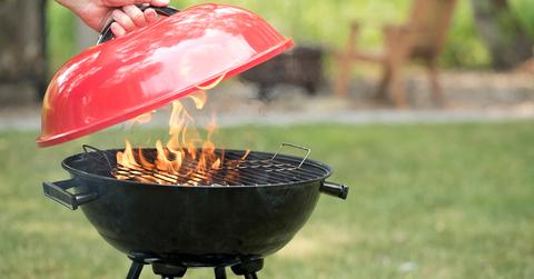 A person lifting the lid of a flaming grill outside.