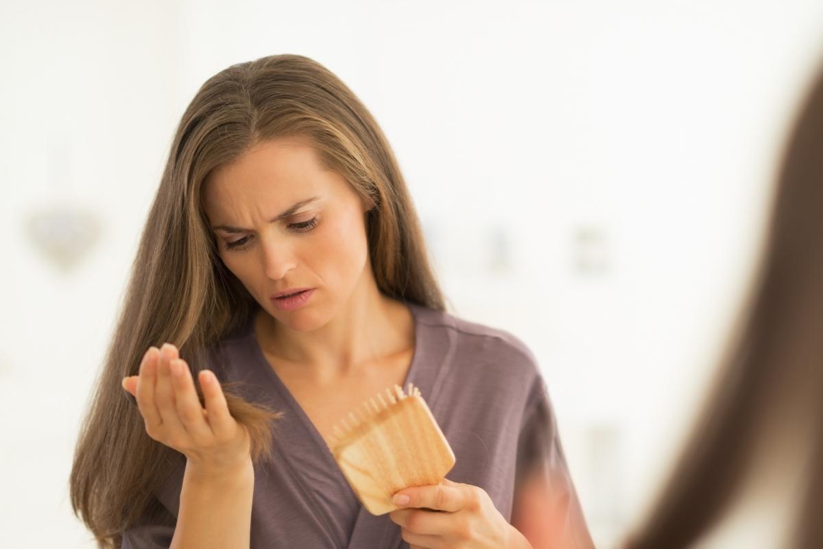 brunette woman looking at hair falling out of brush