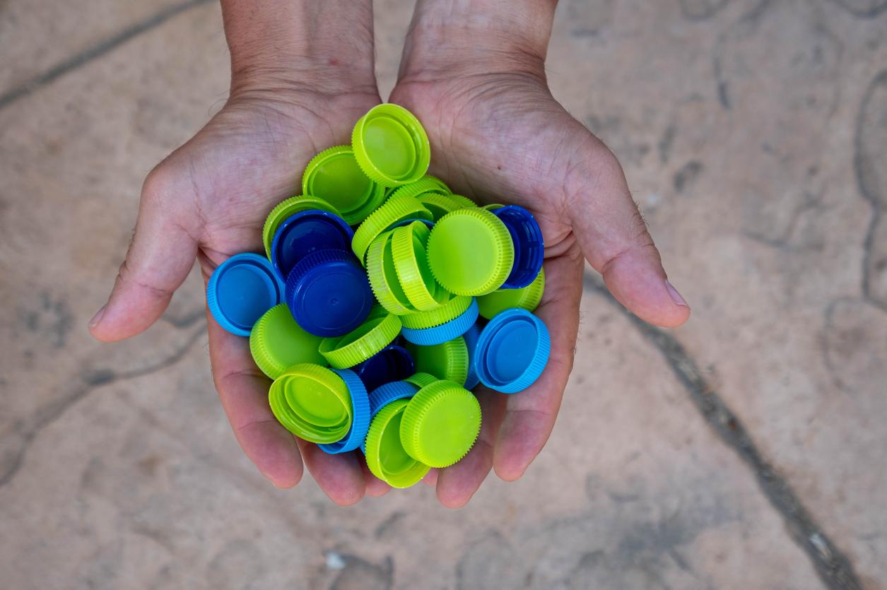 A close up of someone's hands full of green and blue plastic bottle caps.