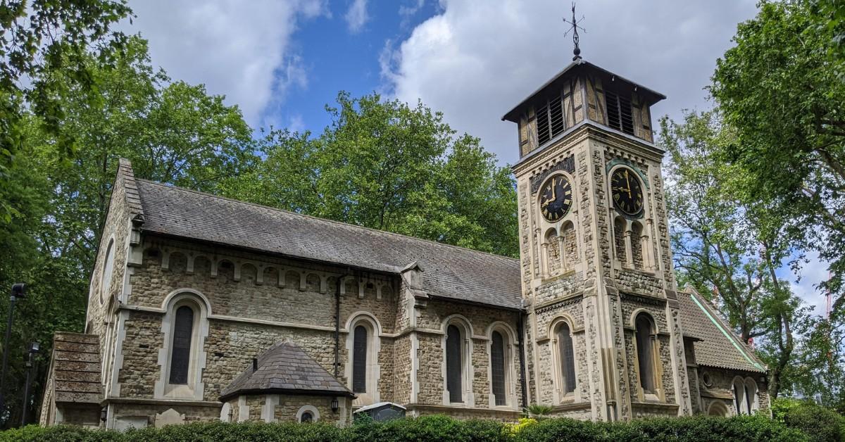 An old stone church is framed by green trees and shrubs
