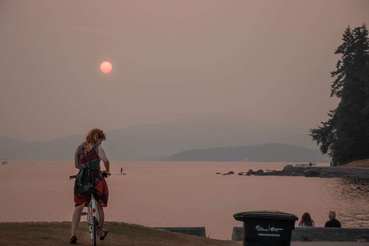 Person on bike near lake with a smoky sky and red sun in the background due to wildfires