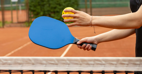 A woman holds a pickleball paddle and ball