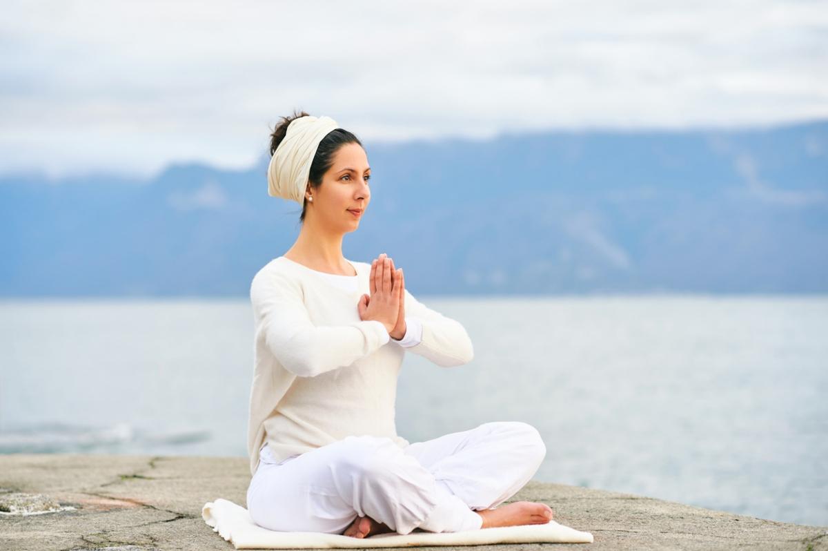 woman wearing white in prayer pose by water's edge