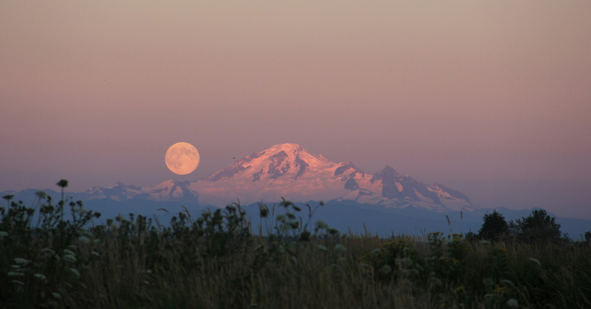 The moon hangs large next to a mountain top