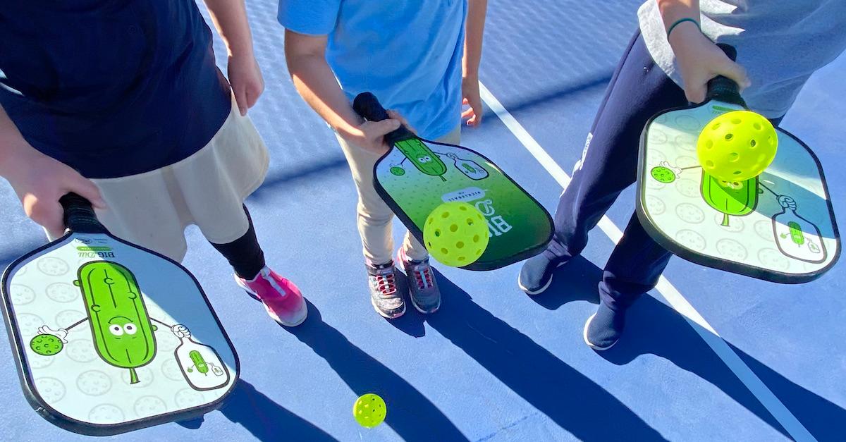 Kids holding pickleball paddles.