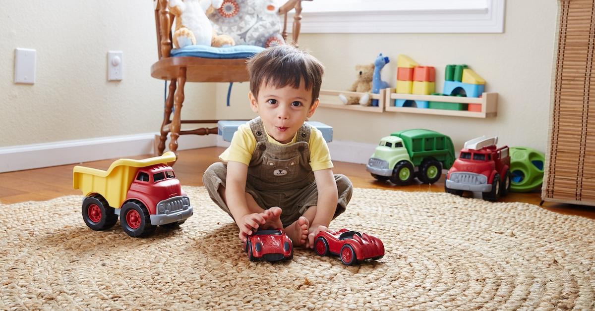 Little boy sits on jute rug and plays with toy cars and trucks.