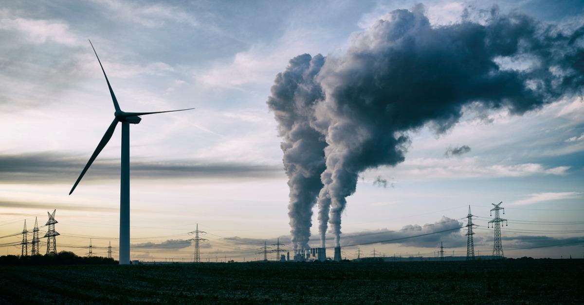 Smokestack from non-renewable energy source next to wind turbine.