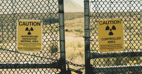 A pair of yellow signs hang on a fence warning people about radioactive material in the area