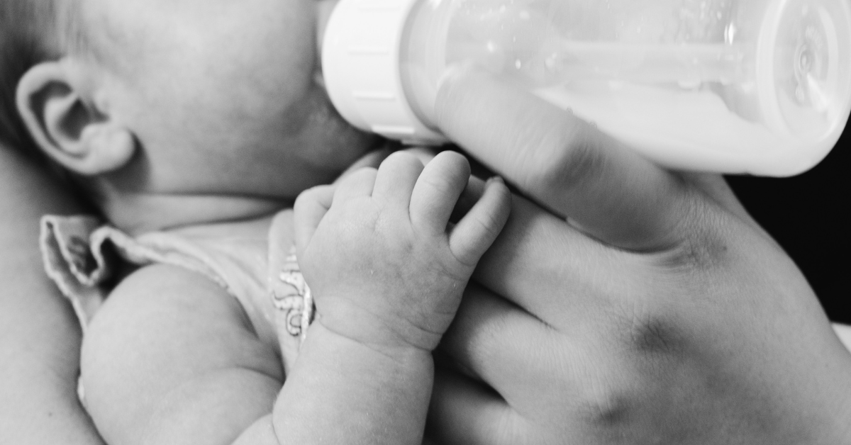 A closeup of a baby drinking formula from a bottle