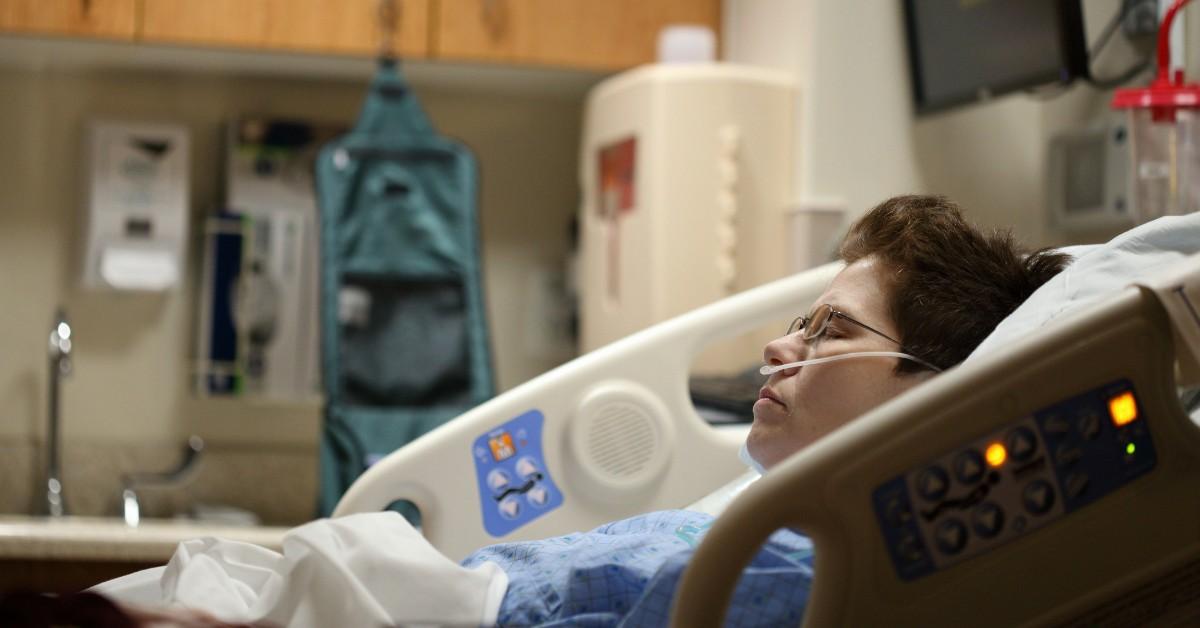 A person lies in a hospital bed while wearing an oxygen canula 