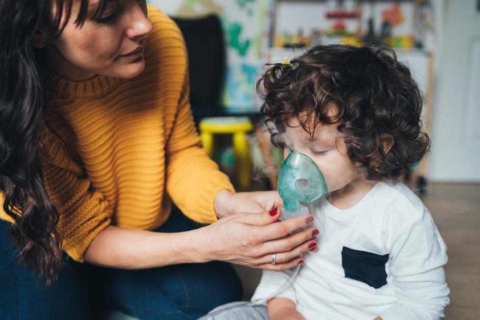 A mother holds up a nebulizer mask to a little boy's face. 