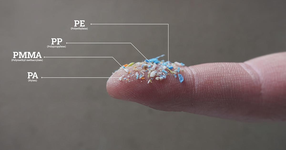 A smattering of colorful microplastics rest on an outstretched finger. The names of four types of plastics are written on the side of the image, with lines going toward the small pile of microplastics.