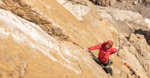 Alex Honnold wears a red jacket and helmet and ascends Pool Wall in Eastern Greenland.