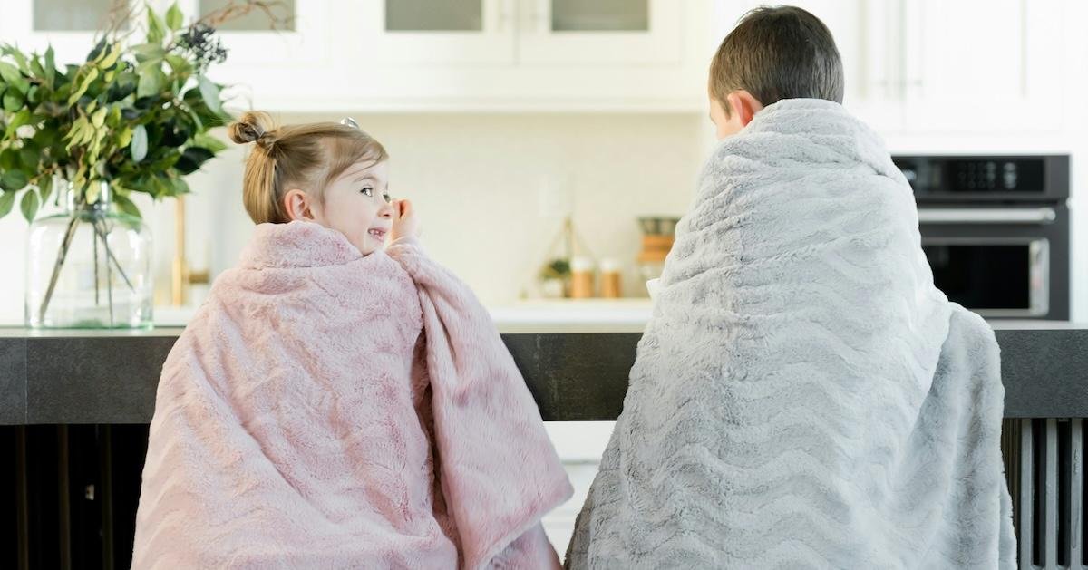 Two kids in electric blankets sit at kitchen counter 