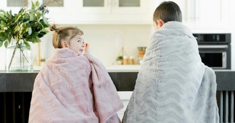 Two kids in electric blankets sit at kitchen counter