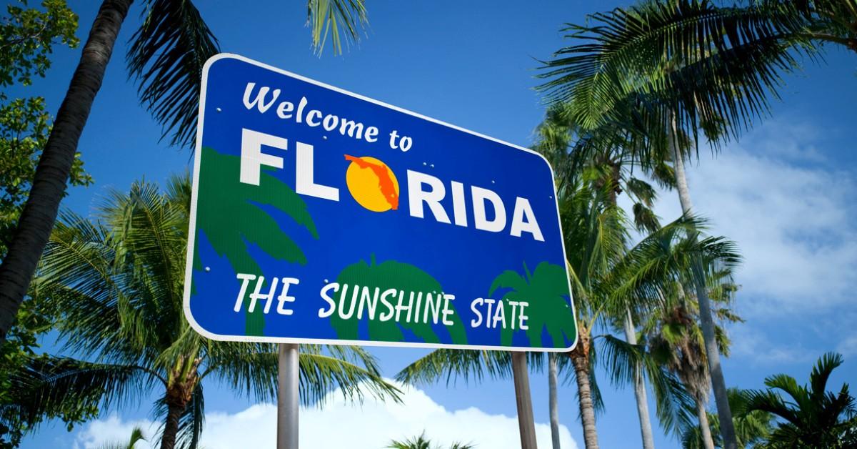 A welcome to Florida sign sits against a blue sky and plenty of palm trees