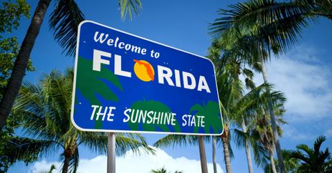 A welcome to Florida sign sits against a blue sky and plenty of palm trees