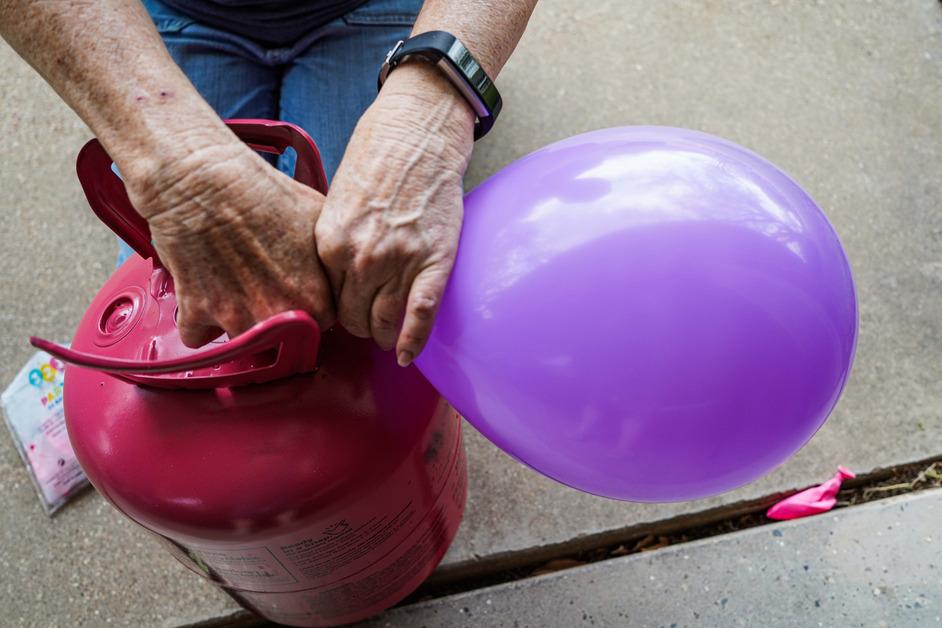 A close-up photo of a senior woman filling up a purple balloon with helium. 