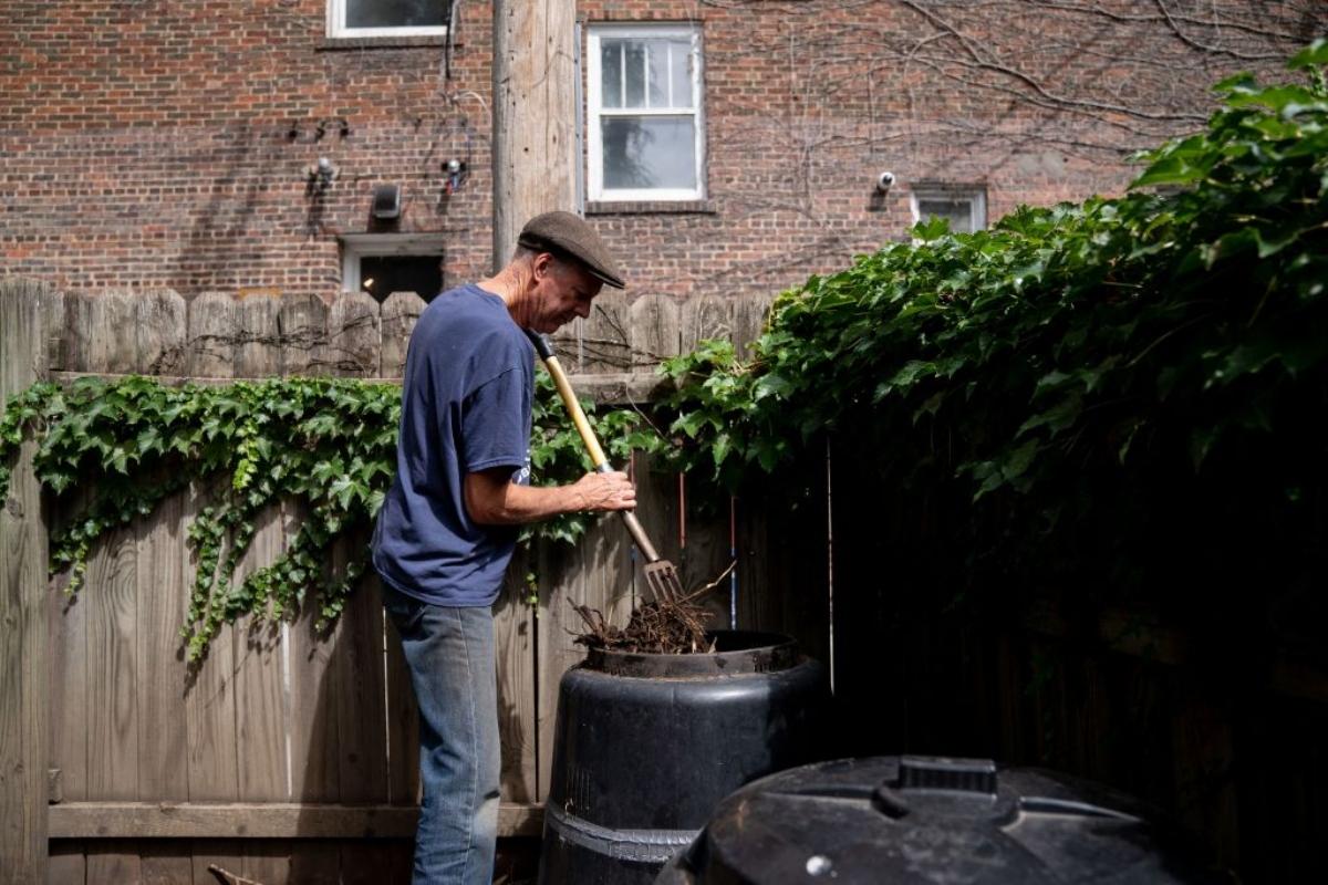 man stirring pile in outdoor compost bin