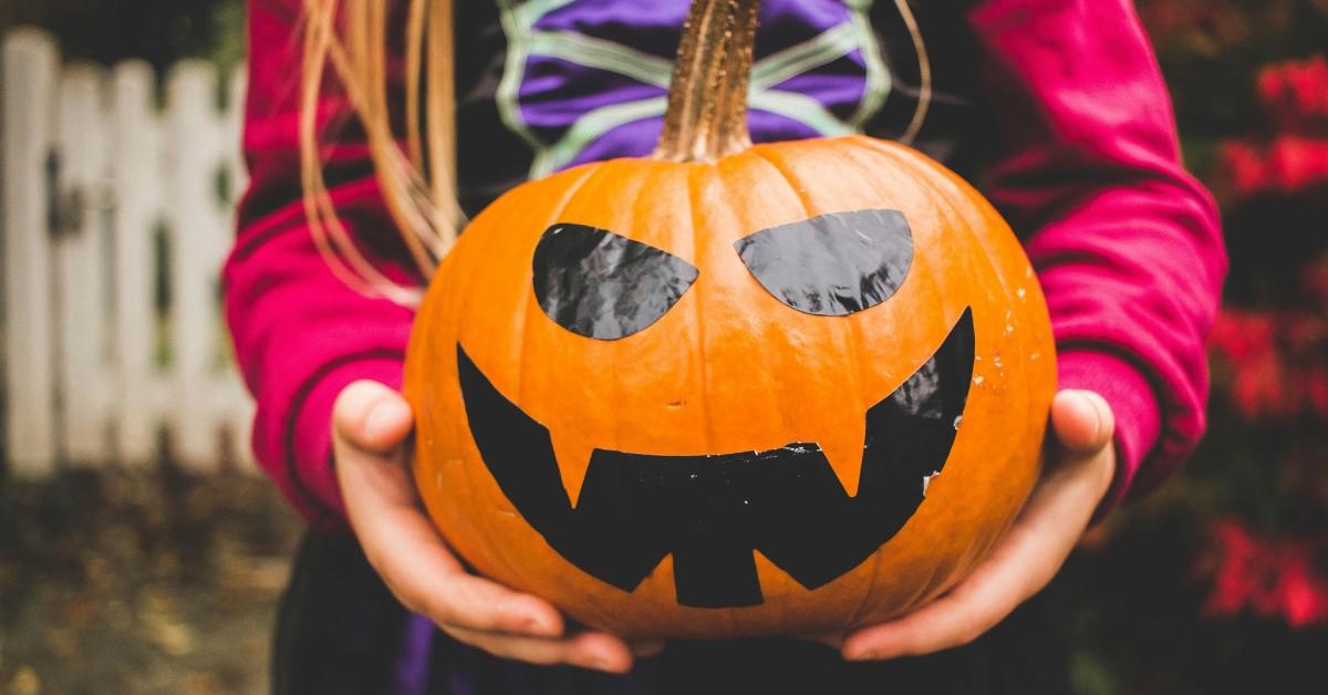 A little girl dressed as a witch holds a jack-o-lantern 